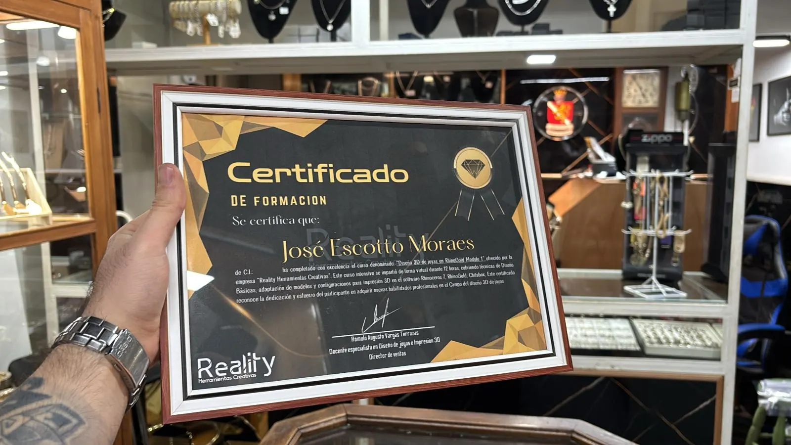 Certificado de formación de Reality Herramientas Creativas enmarcado, a nombre de José Escotto Moraes, sostenido en una joyería